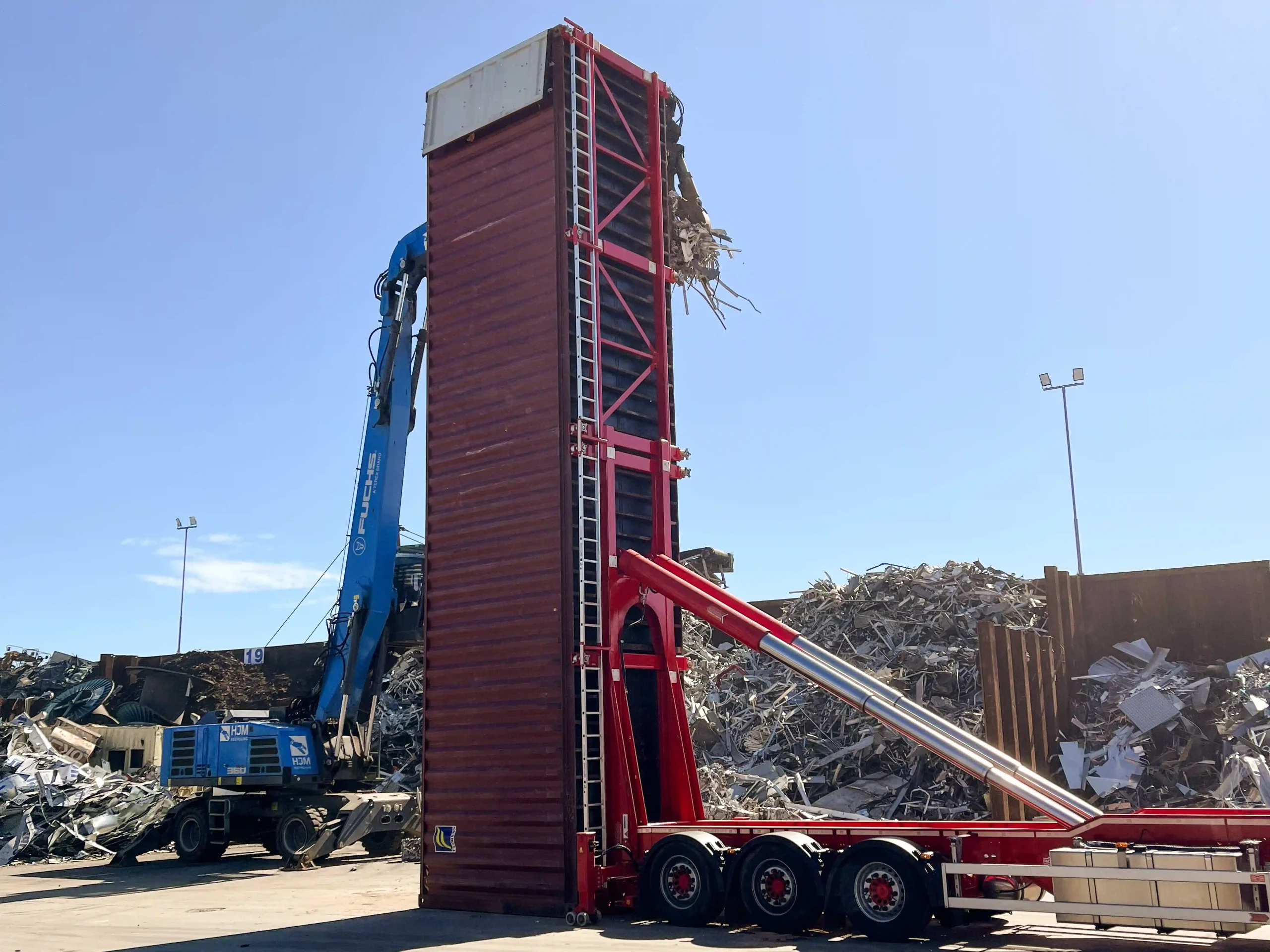 VAKO MVL40 mobile vertical container loader in operation at a scrap metal recycling yard, with a crane loading bulk scrap into a vertically positioned 40ft ISO container