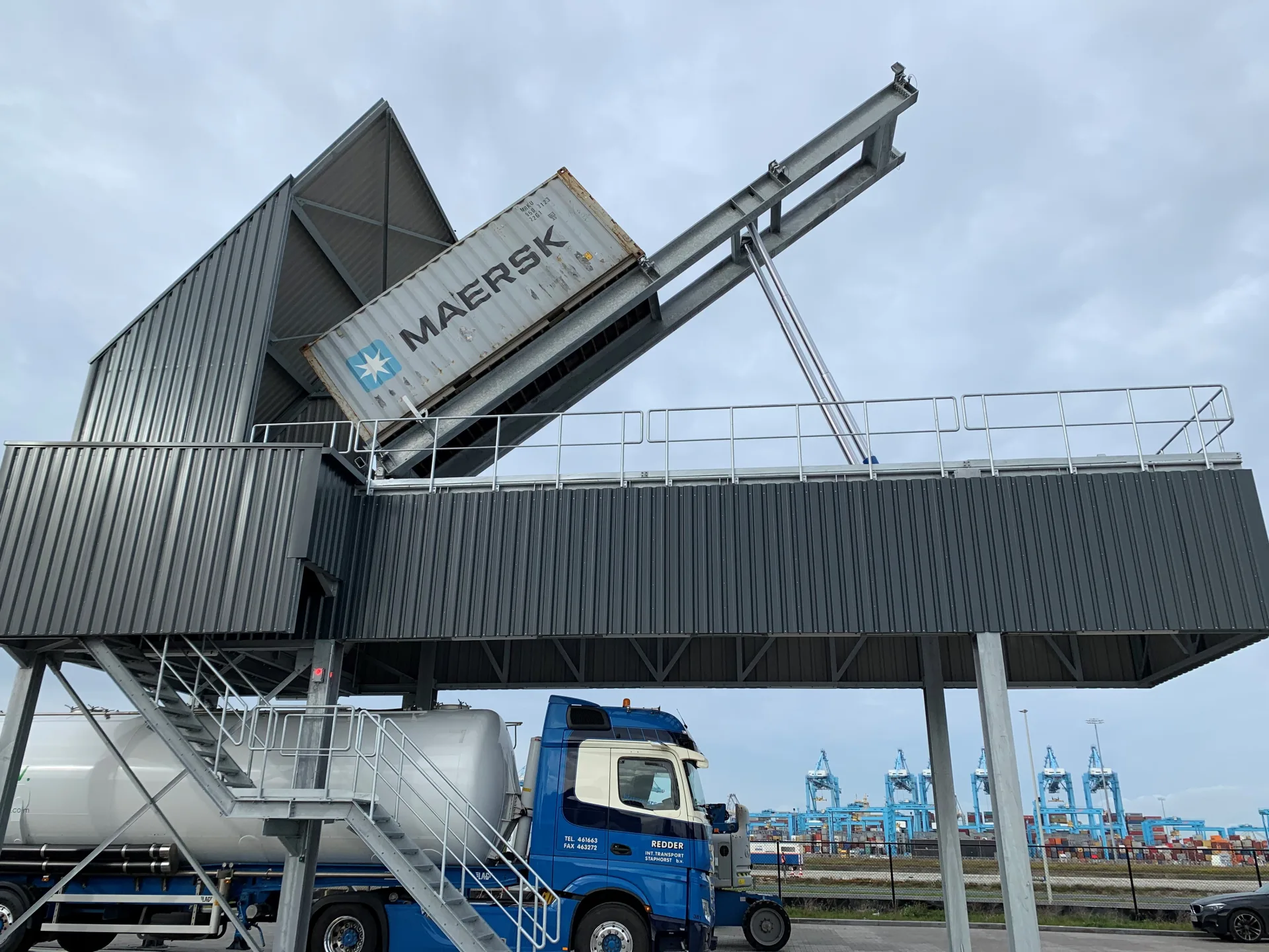 White shipping container raised on the VAKO elevated tipping station above a silo truck.