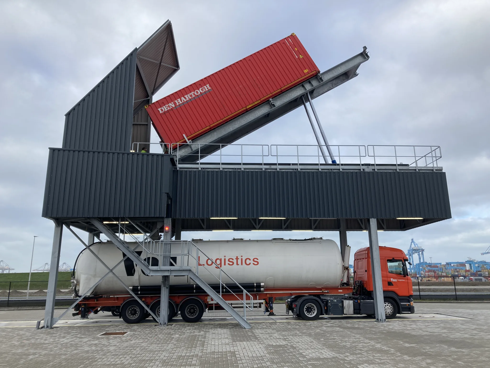 Red shipping container tilted on VAKO elevated tipping station above a silo truck at Maasvlakte.
