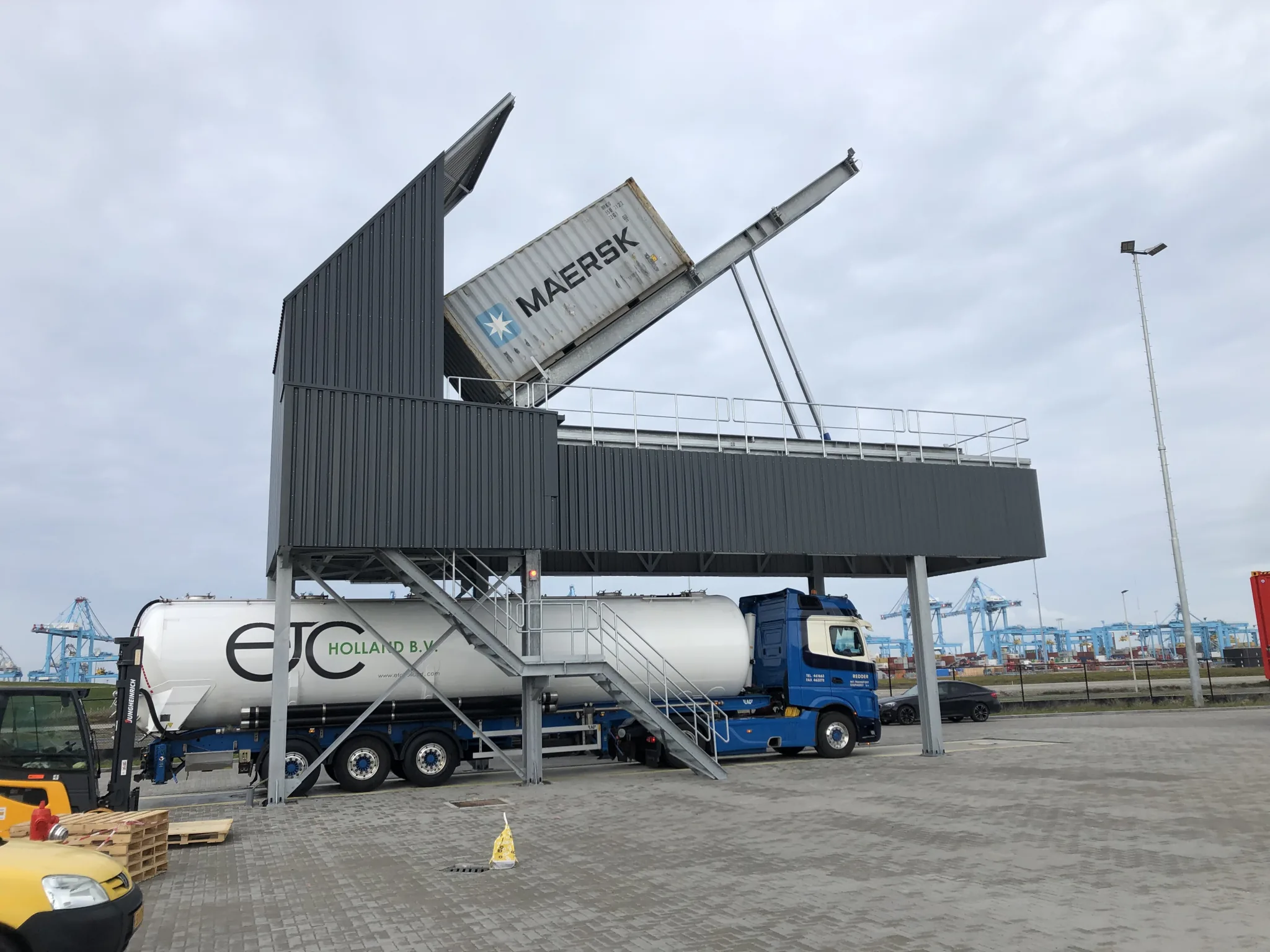 Side view of the VAKO elevated tipping station with a raised container above a silo truck at Maasvlakte.